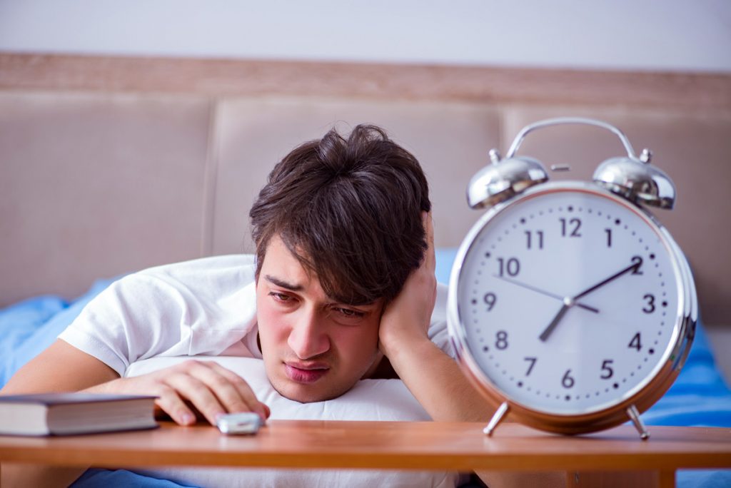 Man in bed frustrated suffering from insomnia with an alarm cloc