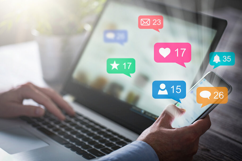 Foto: Hände, Notebook, Mobiltelefon und Social-Media-Icons